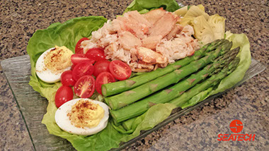 A photograph of a crab Loulie salad with deviled eggs, saparagus, grape tomatoes, artichoke hearts, crab and lettuce.